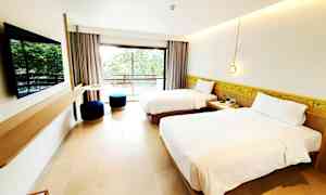 Et hotellrom med to enkeltsenger, en flatskjerm-TV på veggen og en balkong med utsikt over grøntområder. (AI-generert tekst)