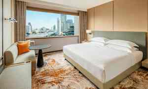 Et moderne hotellrom med en stor seng og en sittegruppe. Utsikt over en by og en elv gjennom vinduet. (AI-generert tekst)