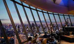 Folk sitter i en luksuriøs lounge med panoramautsikt over byens skyline ved skumring. (AI-generert tekst)