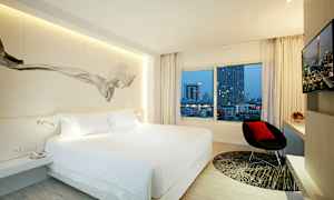 Et moderne hotellrom med en stor seng, et vindu med utsikt over bybygninger, en stol og en TV. (AI-generert tekst)