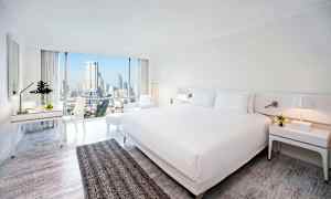 Hotellrom med moderne innredning, stor seng og utsikt over byens skyline gjennom store vinduer. (AI-generert tekst)