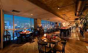 En elegant restaurant med moderne møbler, vinduer som viser en byutsikt om kvelden og belysning som skaper en koselig atmosfære. (AI-generert tekst)