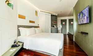 Et moderne hotellrom med en stor seng, hvitt sengetøy og tregulv. En TV er montert på veggen mot sengen, og det er en minibar og et skap i rommet. (AI-generert tekst)