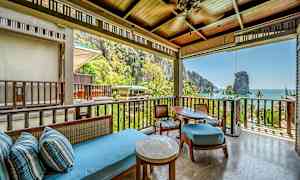 En terrasse med sittegruppe under tak, vendt mot en frodig tropisk natur og havet i bakgrunnen. (AI-generert tekst)