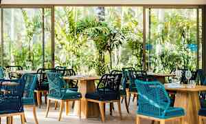 Restaurant med flettede stoler og trebord omgitt av tropisk grønt. (AI-generert tekst)