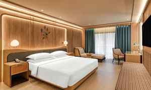 Et moderne hotellrom med en stor seng, nattbord, en lenestol, et skrivebord og et stort vindu med gardiner. (AI-generert tekst)