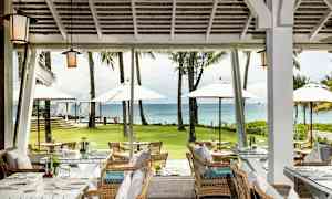 Restaurant med sitteplasser og utsikt over en grønn plen, parasoller og havet. (AI-generert tekst)