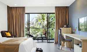 Hotellrom med seng, skrivebord og stoler, samt utsikt mot palmer gjennom en glassdør. (AI-generert tekst)