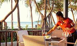 En terrasse med bord og stoler, palmer og havet i bakgrunnen. (AI-generert tekst)