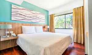 Et hotellrom med en dobbeltseng, store vinduer og gardiner. (AI-generert tekst)