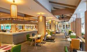 Interiør av en restaurant med bord og stoler i ulike farger samt hengende lamper. (AI-generert tekst)