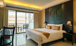 Et hotellrom med en stor seng, skrivebord og en balkong med stoler utenfor. (AI-generert tekst)