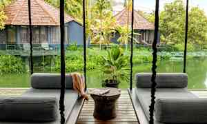 Hengende sittemøbler på en terrasse med utsikt over en frodig hage og små hus med brune tretak. (AI-generert tekst)