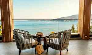 To stoler og et bord står på en terrasse med utsikt over havet og en fjellkyst. (AI-generert tekst)