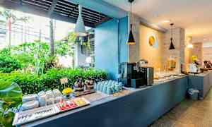 Buffetbord med kaffe, kopper, tallerkener og tropisk grønt i bakgrunnen. (AI-generert tekst)