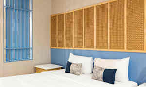 Et soverom med en seng, puter og en blå vegg med flettede paneler. (AI-generert tekst)