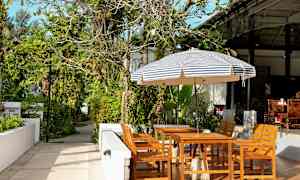 Hagemøbler under en stripete parasoll i en frodig omgivelse. (AI-generert tekst)