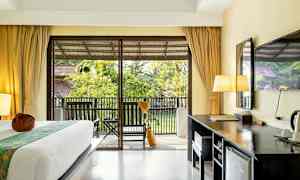 Et hotellrom med en seng, skrivebord og en balkong med utsikt over hagen. (AI-generert tekst)