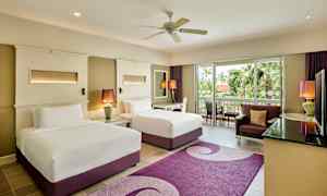 Et hotellrom med to senger, en sittegruppe og utsikt mot grøntområder fra en glassdør. (AI-generert tekst)