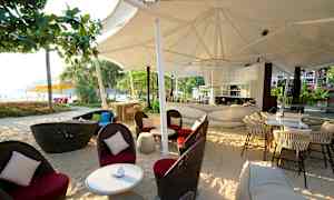 En bar med stoler og bord på en strand under en stor hvit baldakin. (AI-generert tekst)