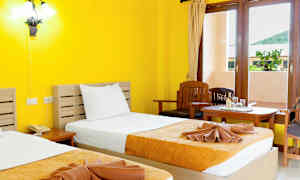 Et hotellrom med gule vegger, to senger med gul-oransje sengetepper, og et vindu med utsikt. (AI-generert tekst)