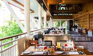 Restaurant med dekkede bord og vinduer med utsikt over grøntområder. (AI-generert tekst)