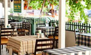 Bilde av en restaurant med rutete duker og bord plassert ute. (AI-generert tekst)