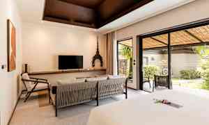 Et hotellrom med moderne innredning, en sittegruppe, en TV, og store glassdører som fører til en frodig terrasse. (AI-generert tekst)