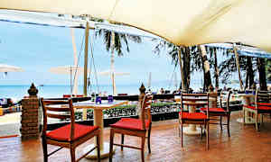 Sitteplasser ved et bord under en markise med utsikt over stranden og havet. (AI-generert tekst)