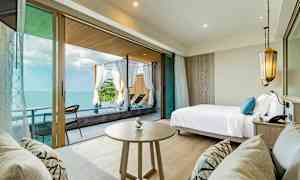 Rom med havutsikt, seng, bord samt sofa og uteplass med solsenger. (AI-generert tekst)