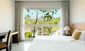 Et hotellrom med en stor seng, et skrivebord og et vindu som viser trær og bygninger utendørs. (AI-generert tekst)