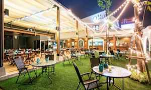 En utendørs restaurant med bord og stoler, plen og lysslynger. (AI-generert tekst)