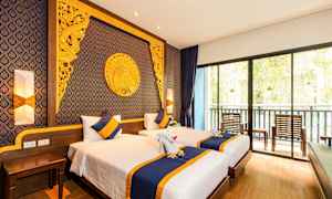 Et hotellrom med to enkeltsenger, dekorert med blått og gult sengetøy og puter. Veggen bak sengene er dekorert med intrikate gyldne mønstre og design. Et stort vindu i enden viser en balkong med stoler og utsikt over vegetasjon. (AI-generert tekst)