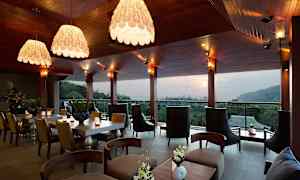 En moderne restaurant eller salong med elegant innredning, store vinduer og utsikt over en skog og åser i bakgrunnen. (AI-generert tekst)