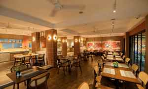 En restaurant med trebord og stoler, dekorert med røde vegger og kunstverk. (AI-generert tekst)