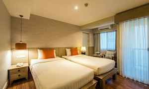 To enkeltsenger med oransje puter i et rom med tre detaljer og gardiner som slipper inn lys. (AI-generert tekst)