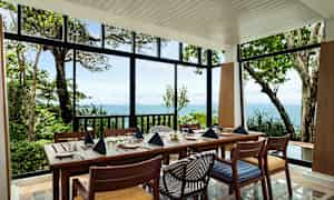 Et dekket spisebord med stoler i en lys paviljong med utsikt over havet og frodig natur. (AI-generert tekst)