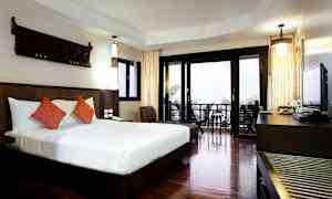 Et hotellrom med en stor seng, to oransje puter, et skrivebord og glassdører som vender ut mot en balkong. (AI-generert tekst)