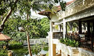 En terrasse i en tropisk hageomgivelse med frodig vegetasjon og en liten dam. (AI-generert tekst)