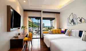 Hotellrom med to hvite senger og gule puter, moderne innredning og balkong med utsikt over fjell og hav. (AI-generert tekst)