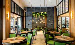 Restaurant med bord og stoler, grønne innslag og dekorative veggdetaljer. (AI-generert tekst)