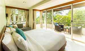 Et lyst og romslig soverom med stor seng, sofagruppe og en balkong med utsikt over grøntområder. (AI-generert tekst)