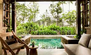 En åpen stue med trestoler og bord, en sofa, og utsikt over en hage og et lite basseng. (AI-generert tekst)