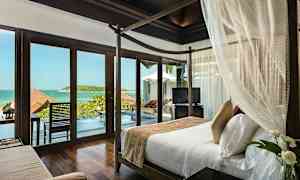 Et soverom med en himmelseng og glassdører som åpner seg mot en utsikt over sjøen og en terrasse med basseng. (AI-generert tekst)