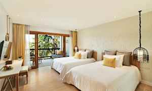 Hotellrom med to separate senger, en balkong med utsikt over palmer, og en sittegruppe. (AI-generert tekst)