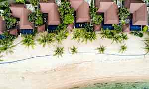 Luftfoto av strandnære bungalower omgitt av vegetasjon og palmer. (AI-generert tekst)