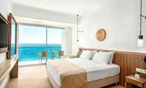 Hotellrom med en dobbeltseng og balkong med utsikt over havet. (AI-generert tekst)