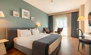 Et hotellrom med en dobbeltseng, to lenestoler ved et bord, et skrivebord og en TV. (AI-generert tekst)