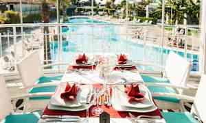 Et bord dekket med røde servietter og hvite tallerkener ved et svømmebasseng. (AI-generert tekst)