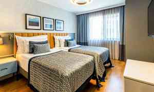 Et hotellrom med to enkeltsenger, moderne innredning og naturlig lys fra et vindu. (AI-generert tekst)